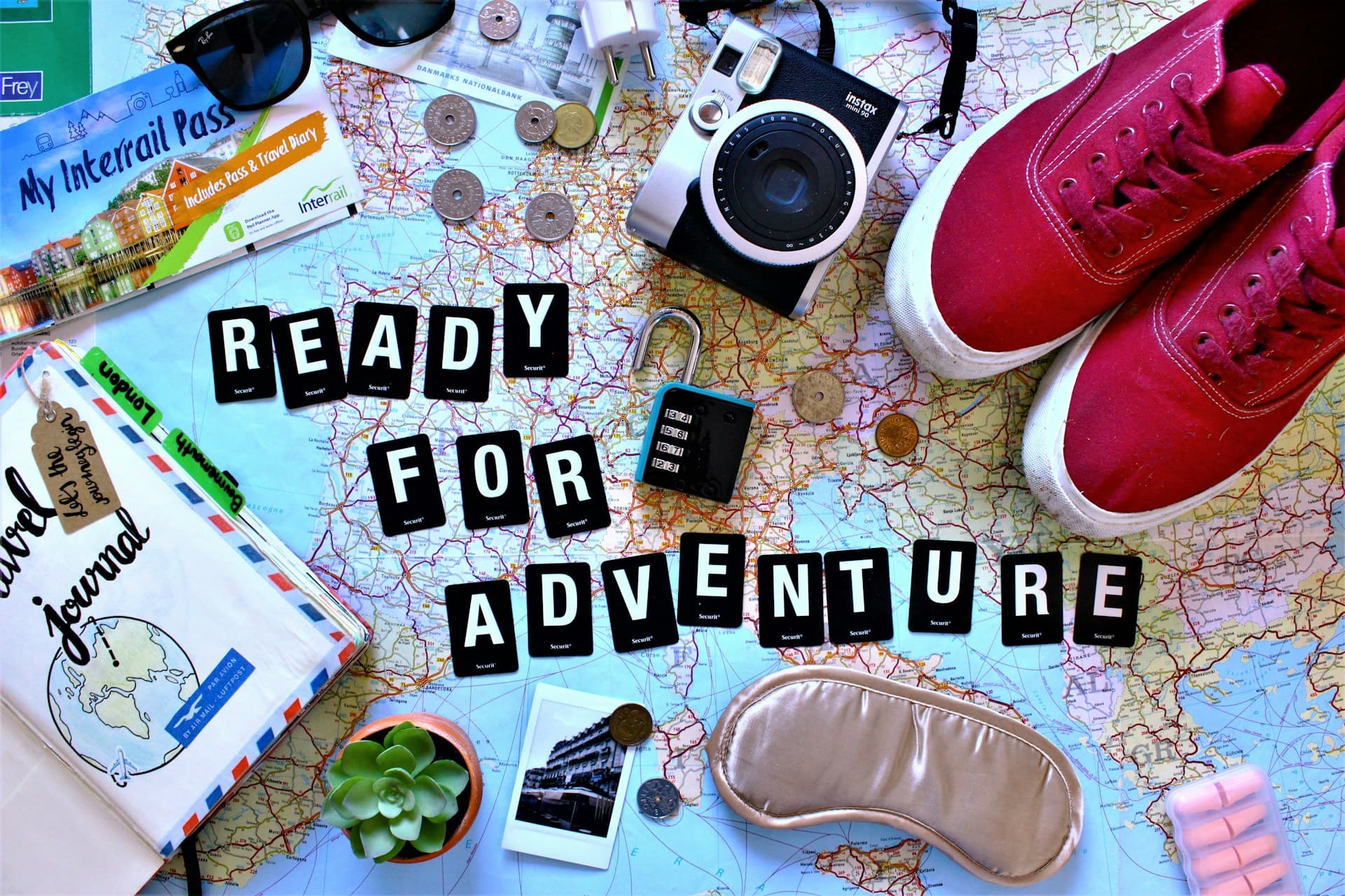Travel essentials on a map, with a camera, trainers and letters spelling Ready for Adventure